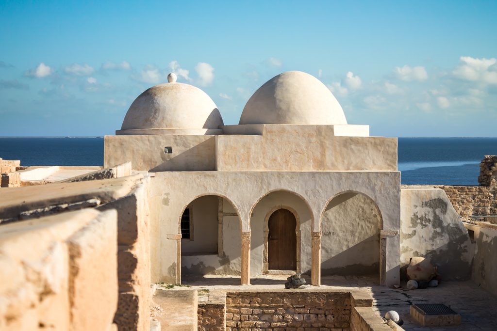 Two whitewashed domes and an arcade inside Borj el Kebir, the sea fort at Houmt Souk, with the sea behind.